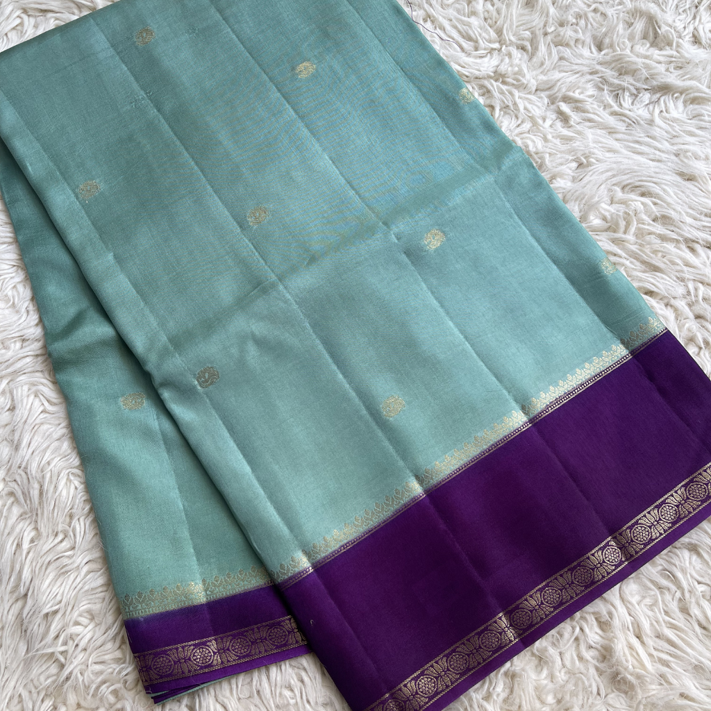 Teal saree with purple border on a white textured background